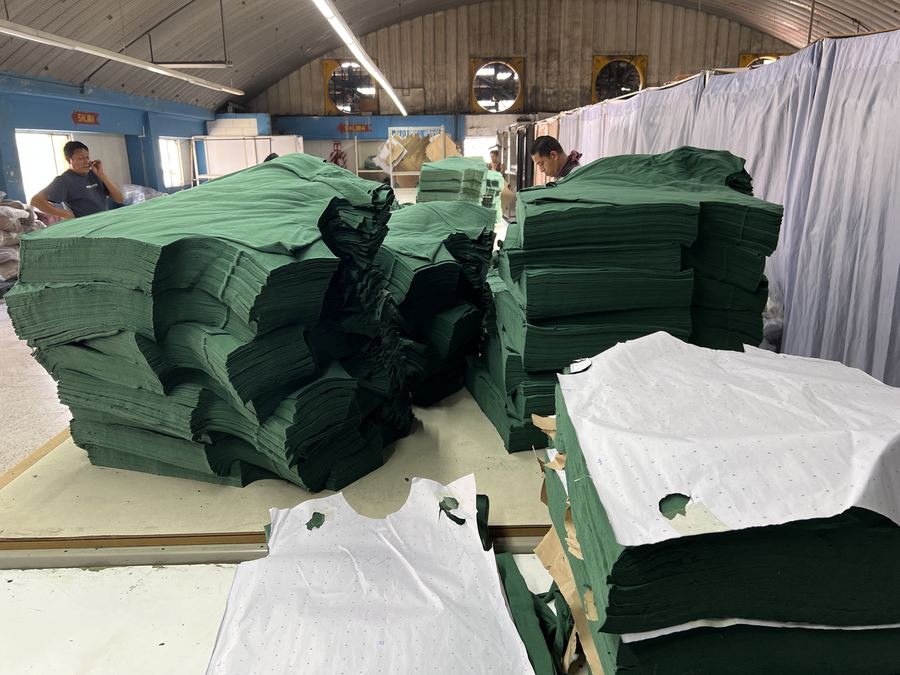 Stacks of cut green knit panels on a cutting table