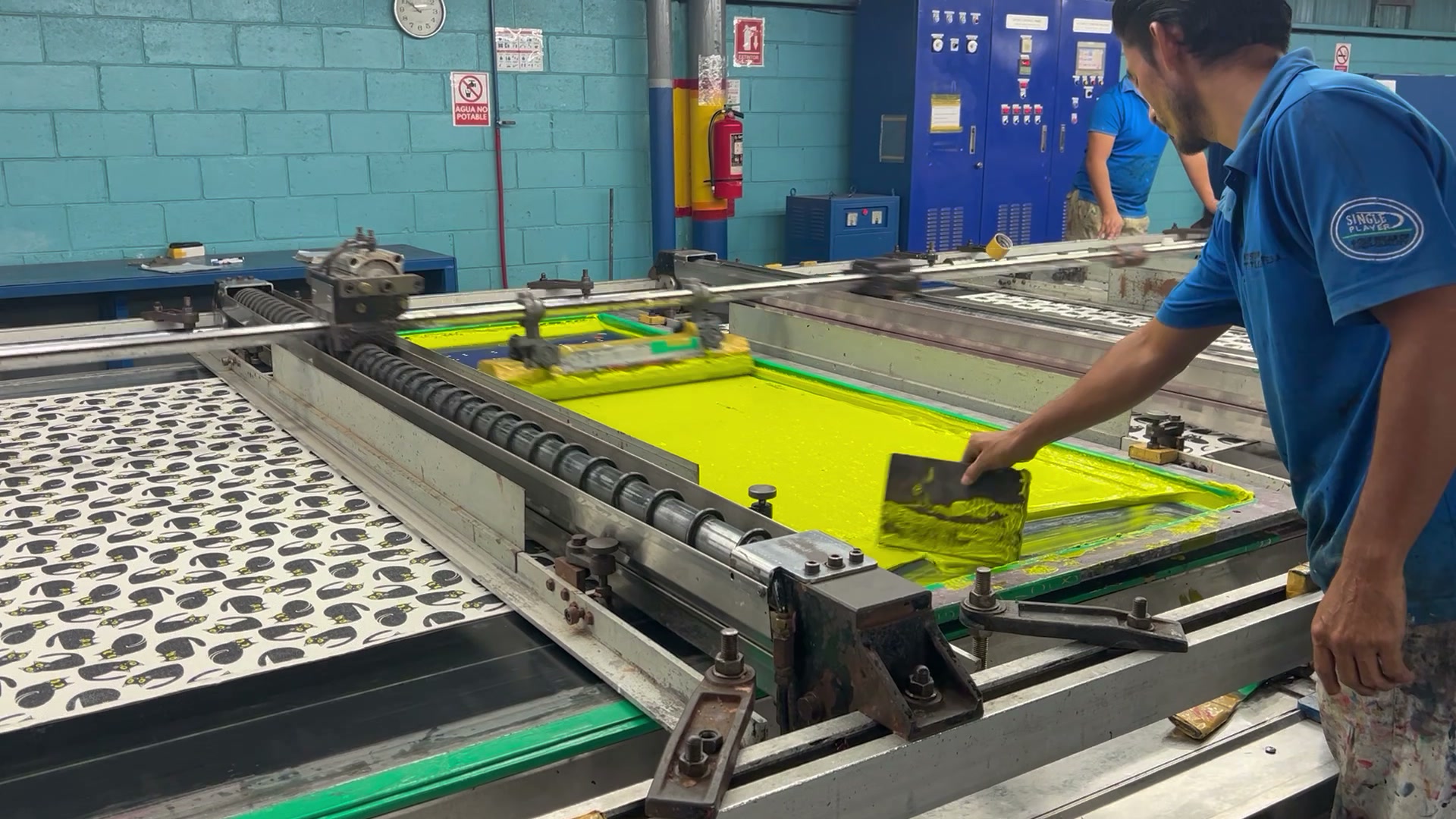 Worker screen printing an allover pattern on a flatbed press
